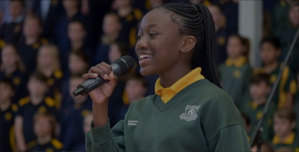 Primary school girl in uniform singing with a microphone